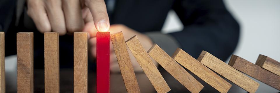 Hand stopping a falling domino to prevent risk escalation, symbolizing proactive risk management and transparency in EB5 investment projects.